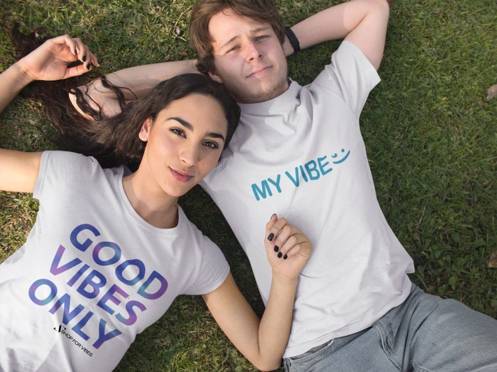 pretty young couple lying down in the park while wearing good vibes t-shirts