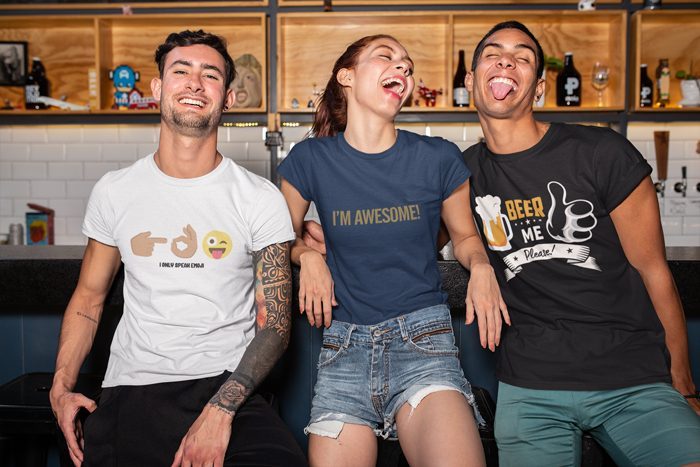 Three friends laughing in a bar wearing I Only Speak Emoji, I'm Awesome and Beer Me Please shirts